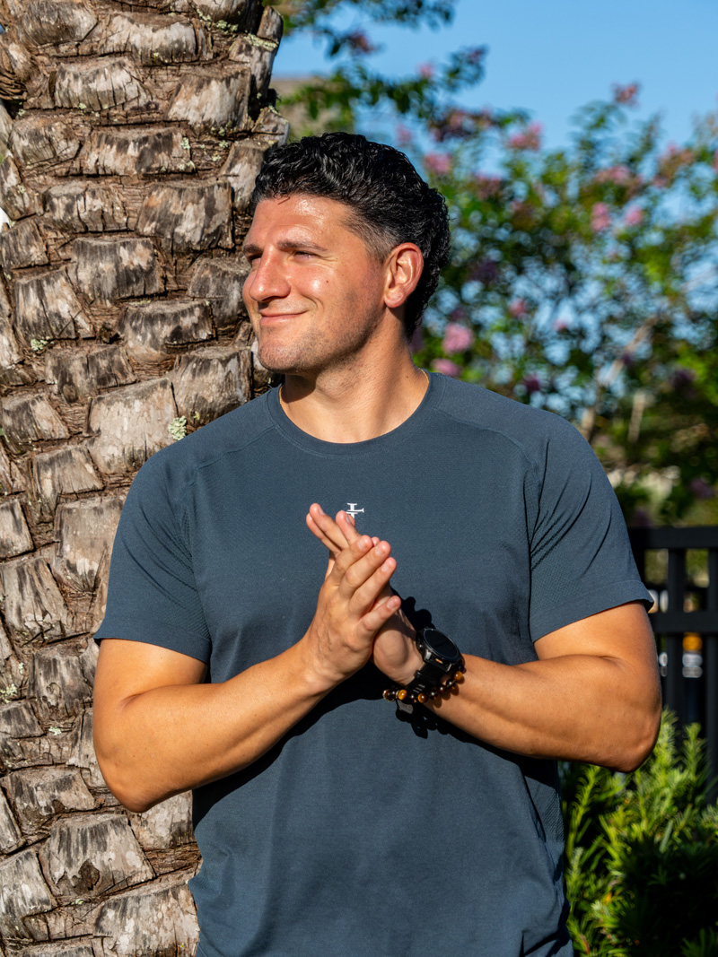 Coach is leaning on a wall and wearing an dark orange jacket.